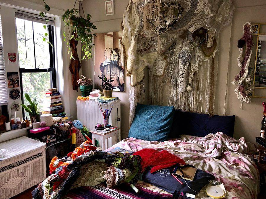 Image Description: Pictured is Dalbey's home studio and work space. Many knitted works are present both on her bed and the walls.  