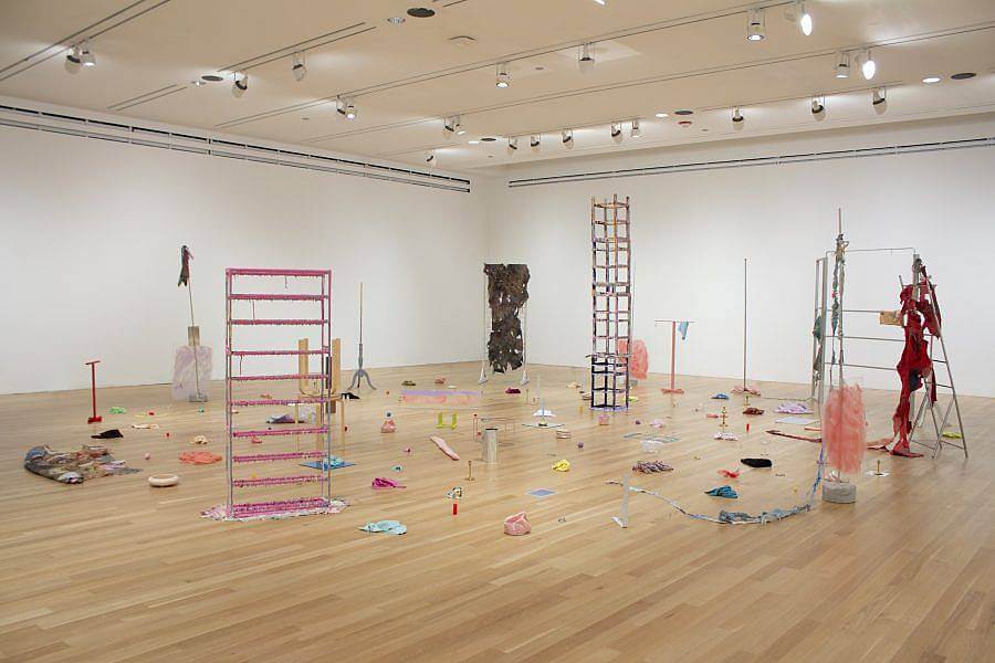 Image description: This is an installation shot of "Wet, Wasted Afternoon", and exhibition held at Logan Center Exhibitions in 2019. The image shows various sculptures made from objects like furniture, household items, and textiles, many of which are painted pink, turquoise, yellow, and red. 