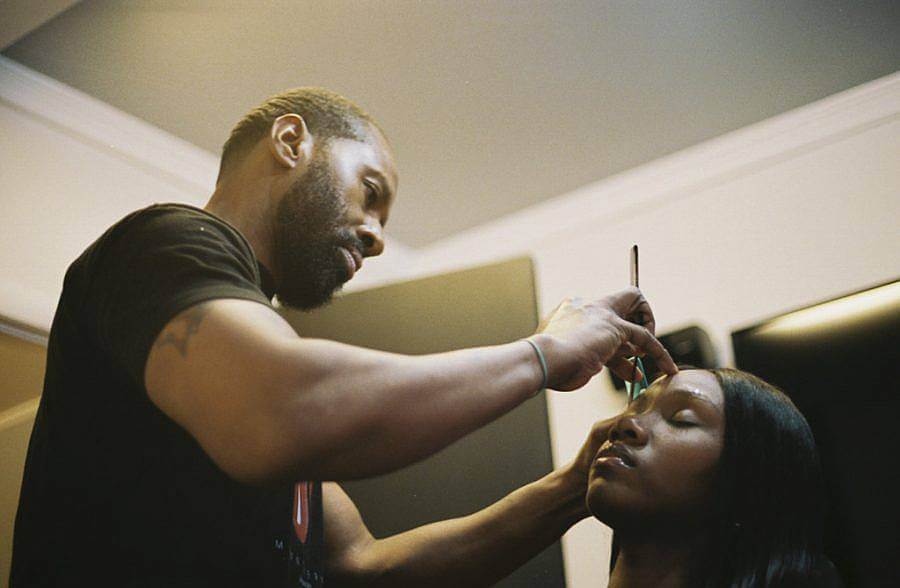 Image Description: This is an photograph of a father arching his daughter's eyebrows. The father looks very concentrated and his daughter has her eyes closed. The photograph has been taken from a low angle looking up.