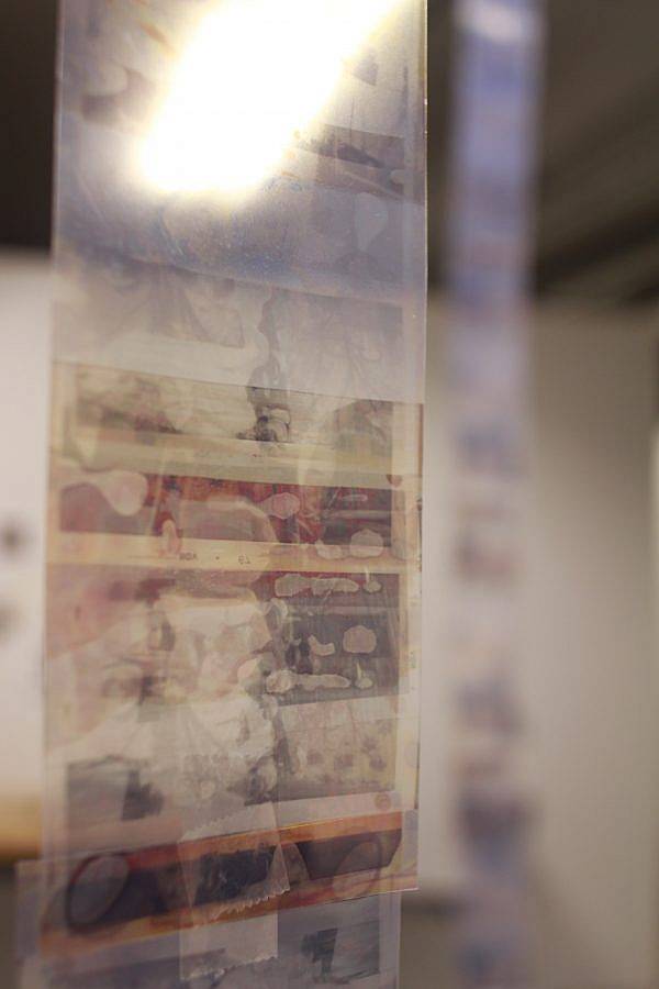 Image Description: This is documentation from a larger installation of floor-to-ceiling reels of layered deteriorated prints. This is a detail shot of one of the reels. The images are in shades of tan and printed on a transparent material.