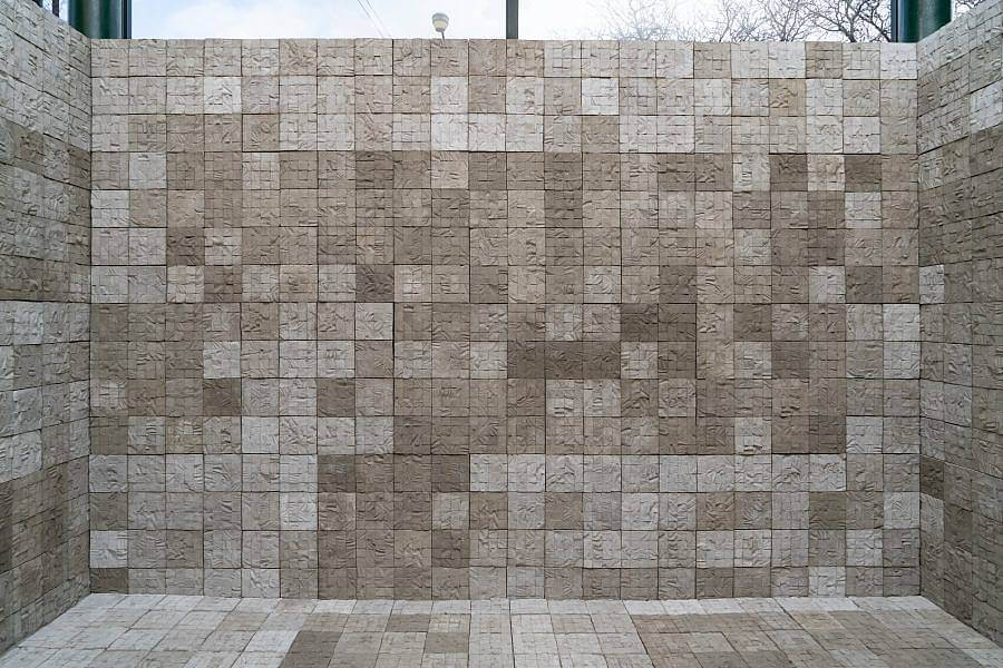 Installation view of cement tiles that make up a room. The walls and floor are both made of a serialized cement tile structure.The back wall is on display. The tiles which are textured with the skin of human donors, are 6 inch squares. The walls are 17 squares high and 25 squares across. A window can seen behind the wall. 