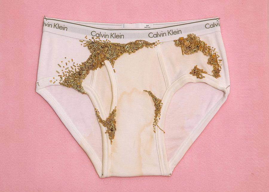 A pair of Calvin Klein underwear is depicted against a pink background. gold beads are embroidered on the urine soaked underwear. 