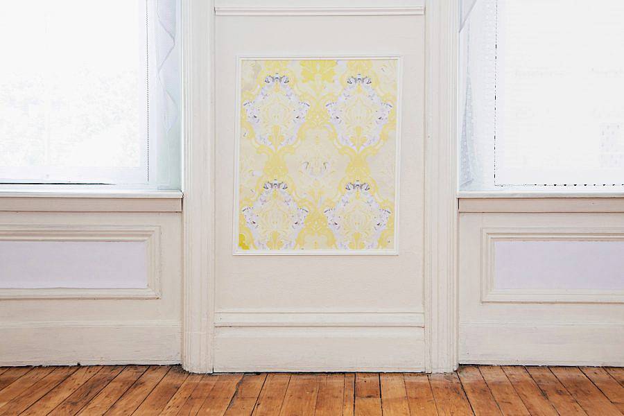 Detailed shot of artist’s exhibition Indecent Exposure. The photo shows an image of a wall between two images. On the wall is rectangle of an ornate yellow wallpaper. 