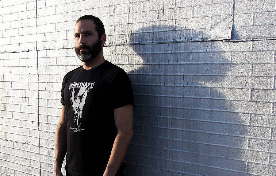Photo of Josh Cheon against a brick wall. He wears a mineshaft shirt. He is a white man with a beard and close cut hair. 
