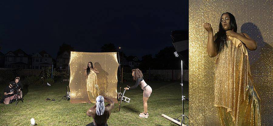 Two images against one another. The Left features a a photo shoot set up at night. A gold backdrop is set up. Dion, a black nonbinary person, with long black hair, wearing glasses, is wrapped in a golden fabric against the backdrop. There are production assistants featured in the image. To the right is a close up of, Dion, it appears to be the same image from the left.