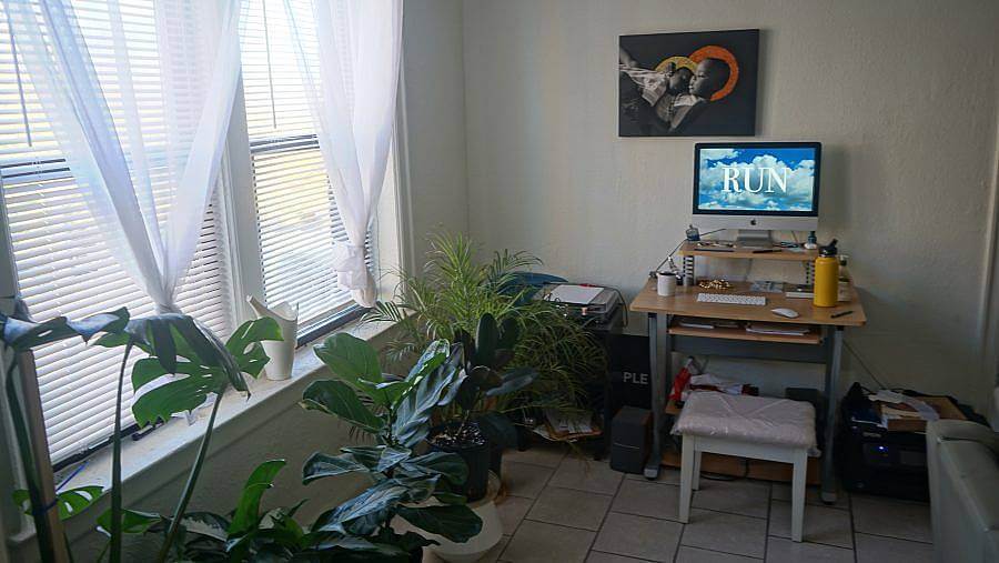 Photo of artist's studio space, featuring monsterra plants, a desk, and a desktop computer. The background of the screen reads "RUN."