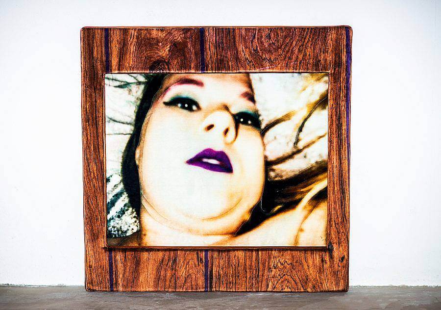 A close of image of artist Sarah C Blanchette of her face, lips, chin, against a pillow. The image is framed by a wood panel. 