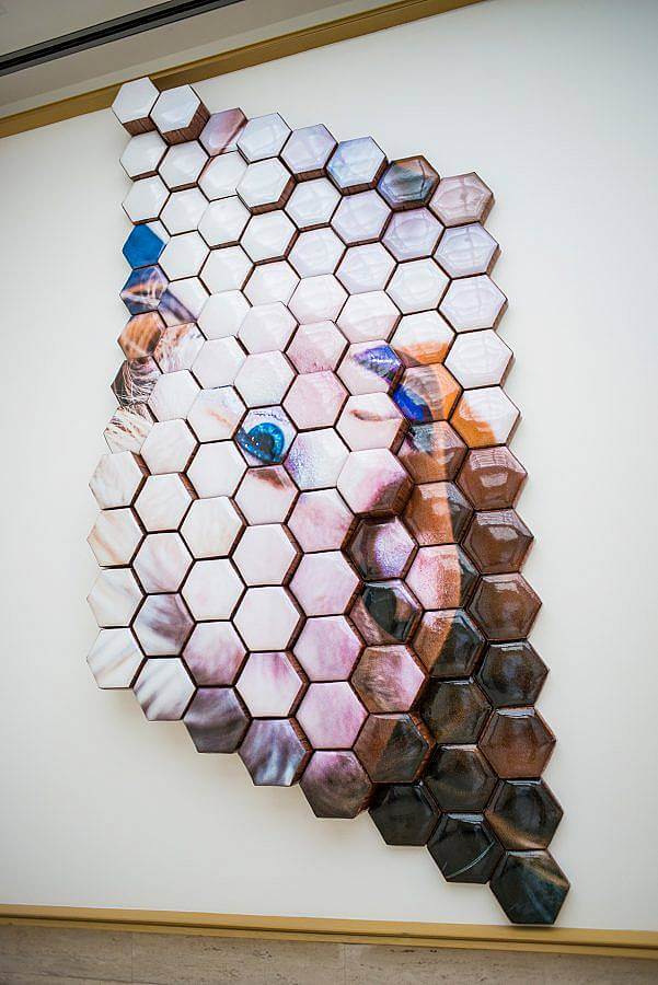 Hexagon fabric shapes form a rhombus. They are arranged in varying depths. An image of the portrait of the face of the artist is displayed upside down. She wears purple lipstick. Her eyes are saturated blue.