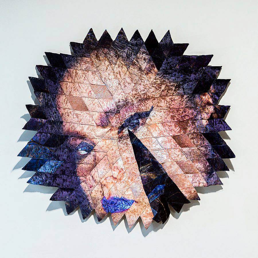 An image of a woman is displayed in a series of diamond shaped iridescent velour fabric pieces. The fabric pieces form a circular form, with their points, pointing outward. 