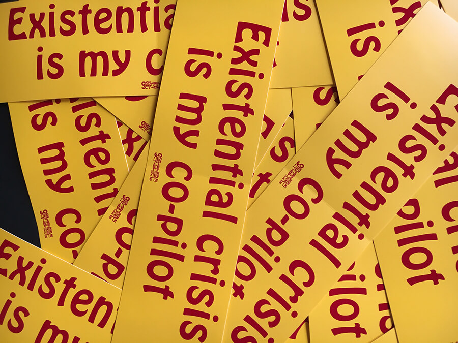 A photo of text-based bumper stickers all laying atop one another. Each reads "Existential crisis is my co-pilot."