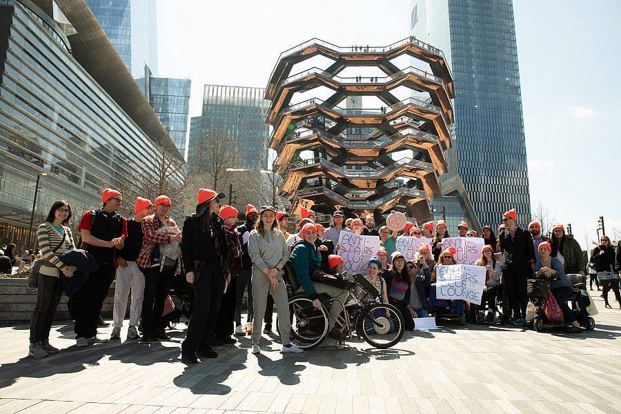 Image description: About 40 people posed in front of the Vessel sporting neon orange, Anti-Stairs Club Lounge beanies and holding Anti-Stairs Club Lounge Signs.