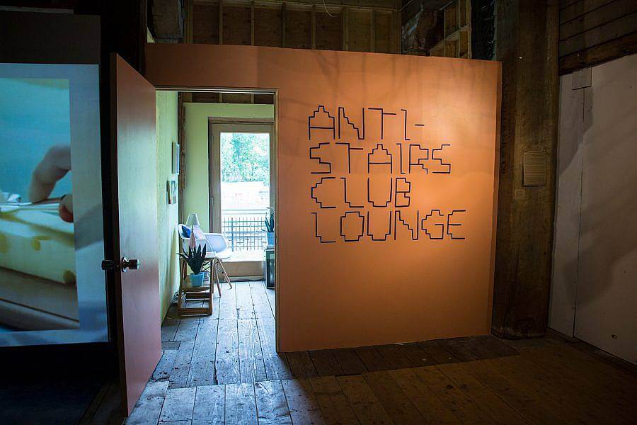 Image description: An orange wall with big text in a stair-inspired font that says, "Anti-Stairs Club Lounge."