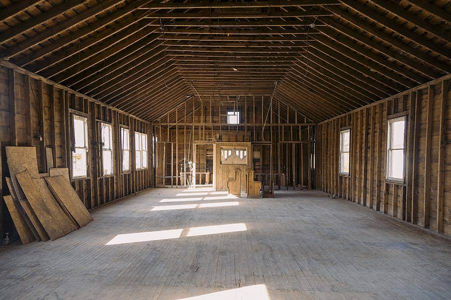 Image description: A stripped down all wooden interior of a building is displayed. Natural light pour in through the windows. 