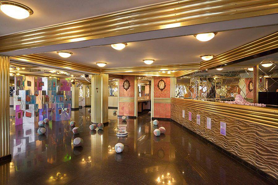 Image description: Installation view of a design space with a shiny marble floor. Gold metal moldings are visible. Sponge objects are strewn about the floor. 