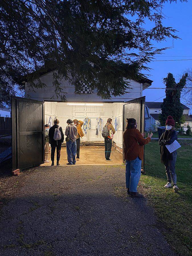 Image Description: This is a photograph of the opening at the gallery in early event. There are various people looking at the work inside the gallery and two people having a discussion outside. All visitors are masked.