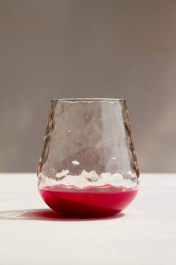 Image Description: This is a stemless translucent wine glass with a tan tint. The glass is dimpled and is filled with a small amount of red wine.