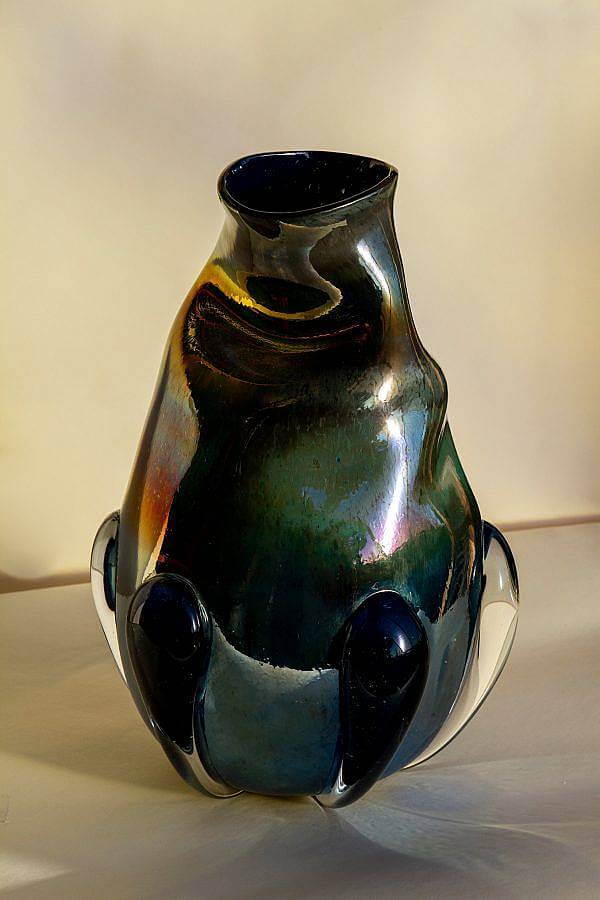 Image Description: This is a large dark green and blue vase with a holographic surface. There a large masses of fully clear glass towards the bottom and the top of the vase is folded over slightly.