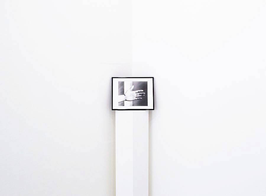 Image Description: This is a framed photograph of a hand sitting on a pedestal. The photograph is propped up against the corner of the wall. There is a beam of light moving down the center of the hand.