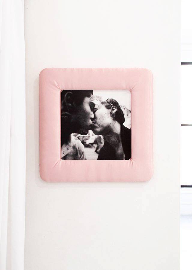 Image Description: This is a black and white image of two people kissing. There are two kiss marks on the image. The photograph is framed in a pink satin frame.