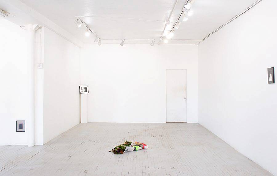 Image Description: This is an installation shot of the gallery. There are three photographs both on the walls and on a pedestal. There are two bouquets of flowers wrapped in photographs and ribbons on the floor. 