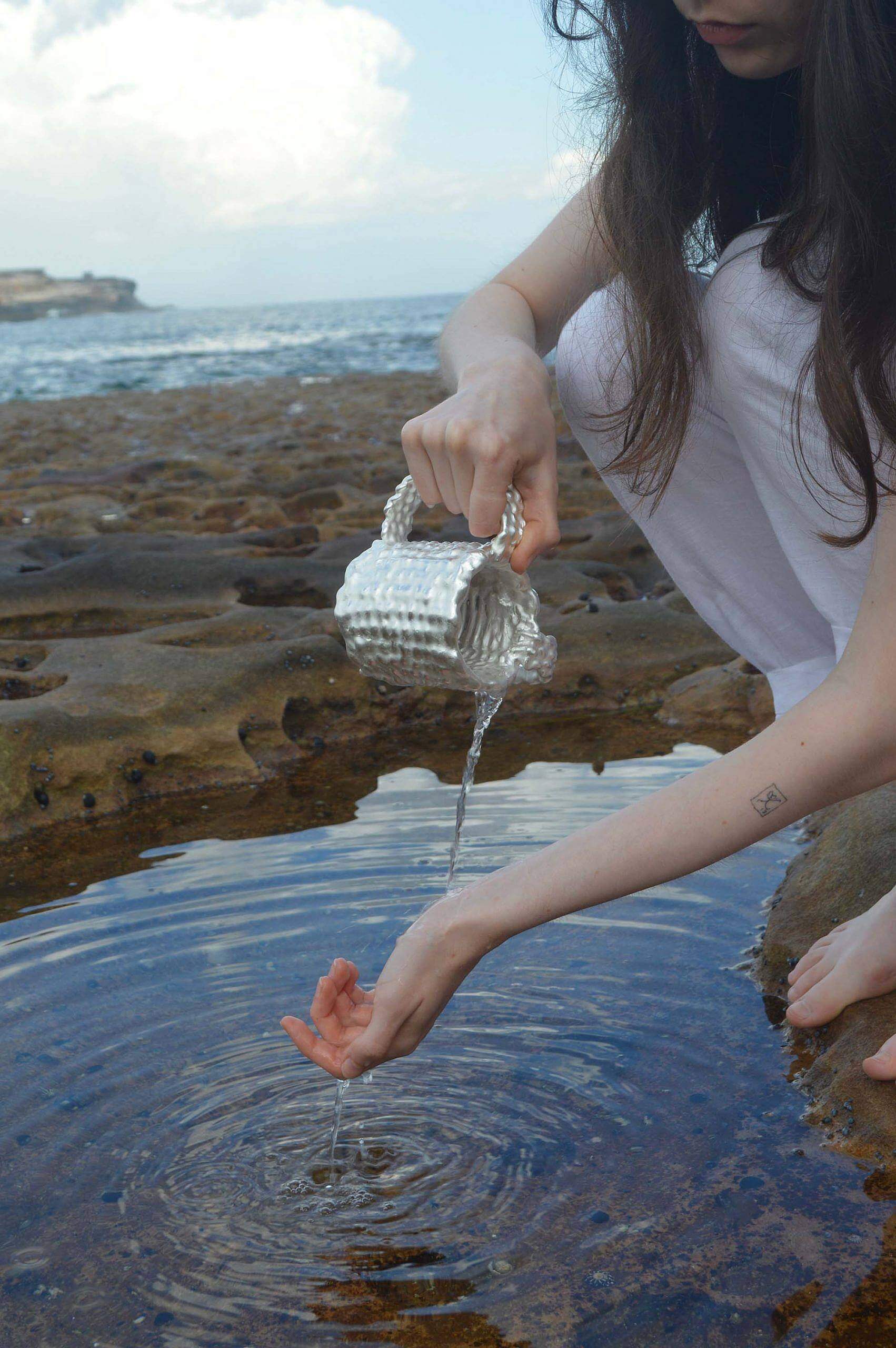 person pouring water onto their hand out of a silver cup